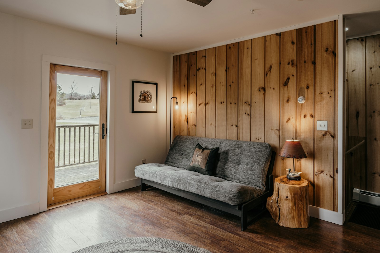 Small rental bedroom with a futon, pine wall, and deck door