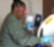 Woman in pink glasses and blue gloves cleans a white hospital bed in a medical room, with a machine visible in the background.