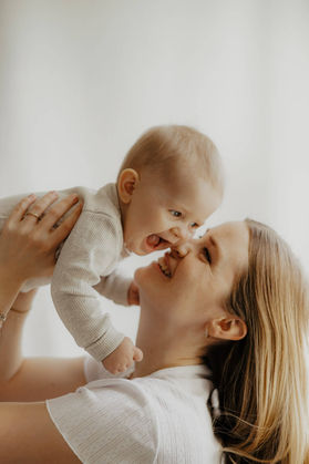 Mor kysser sin smilende baby i lyst dagslysstudie – babyfotografering i naturligt lys