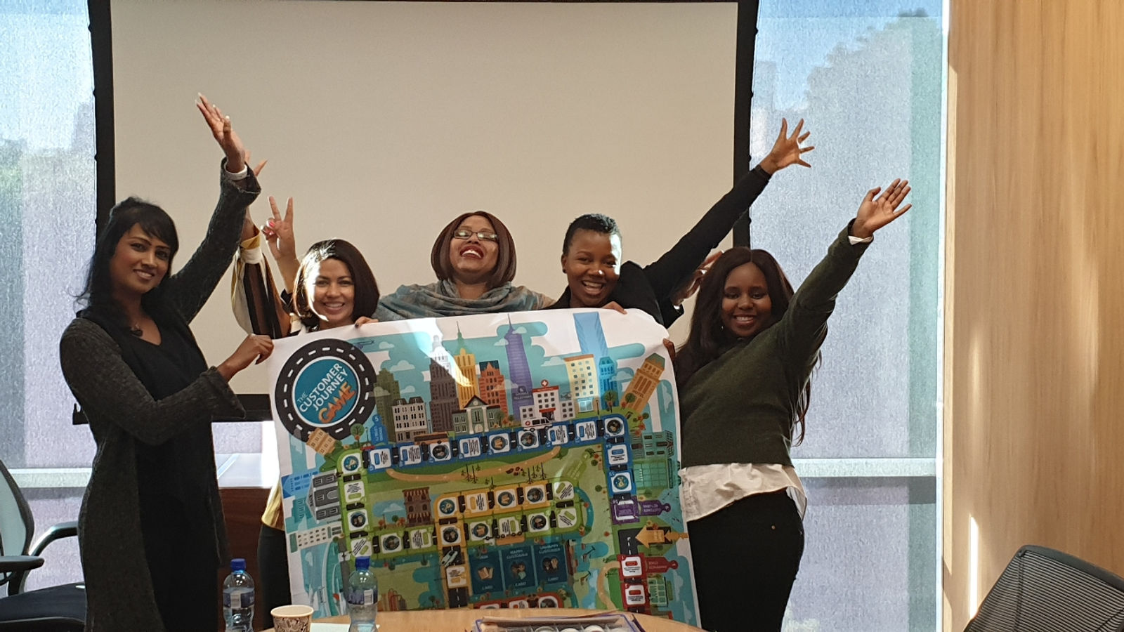 A winning team holding up their Customer Journey Game board with arms raised in celebration