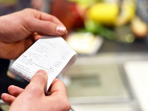 Pessoa segurando uma folha de papel com preços e itens listados, em um ambiente que parece ser um restaurante ou loja.