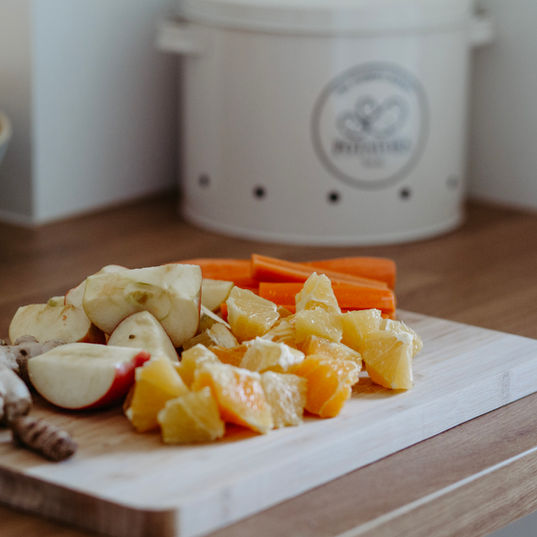 In der Küche steht ein Brett mit kleingeschnittenem Apfel, Orangen, Kurkuma und Möhren