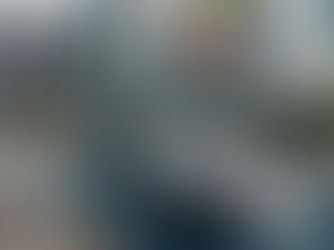 Dual monitors display video editing software; a guitar, dancer, and saxophone appear. Desk has keyboard, headphones, plants, and pens.