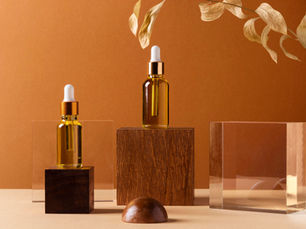 Two amber dropper bottles on wooden blocks against a warm brown background. Dried leaves hang above, creating a natural, serene vibe.
