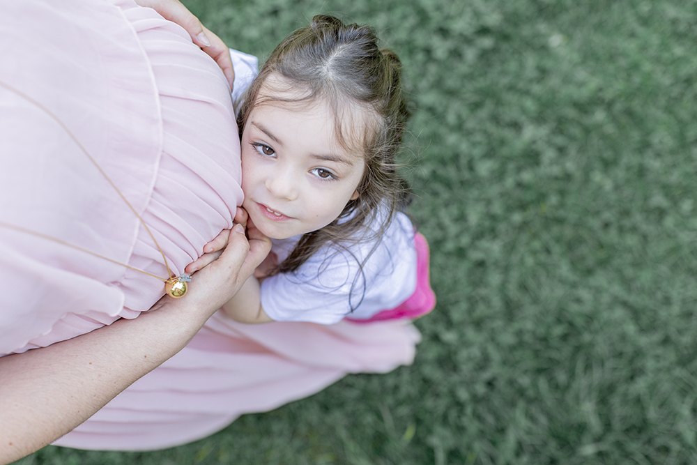 Eva qui fait un câlin au ventre arrondi de sa maman qui attend un deuxième enfant