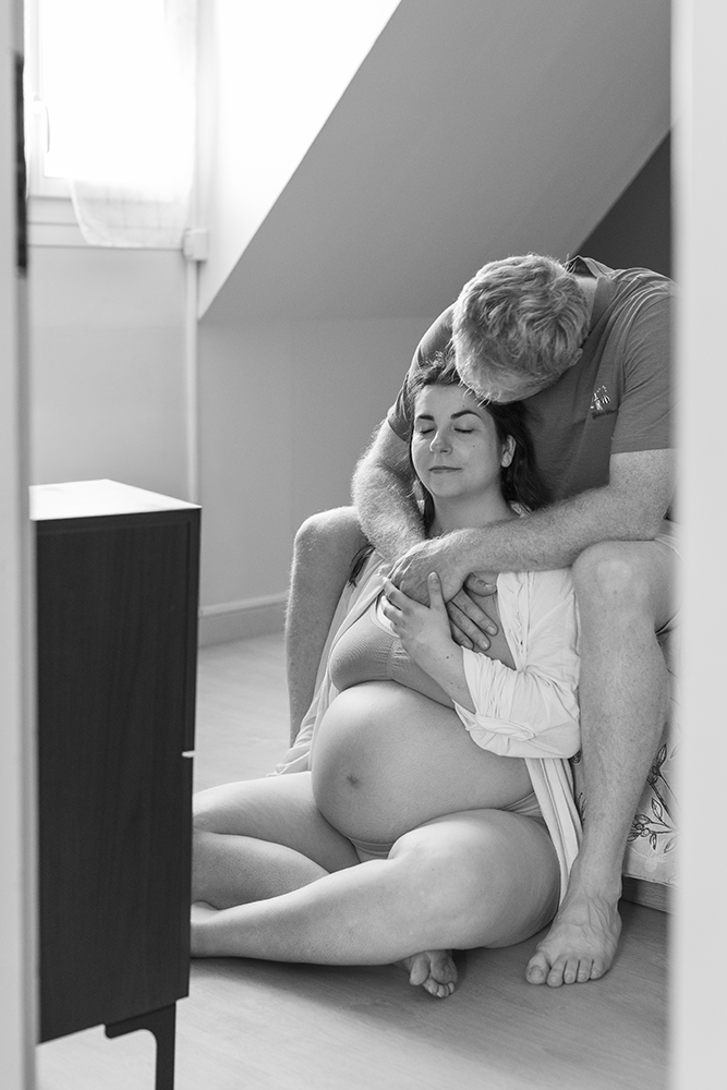 Le couple de futurs parents s'enlaçent dans la chambre à coucher lors de leur séance grossesse à Haguenau