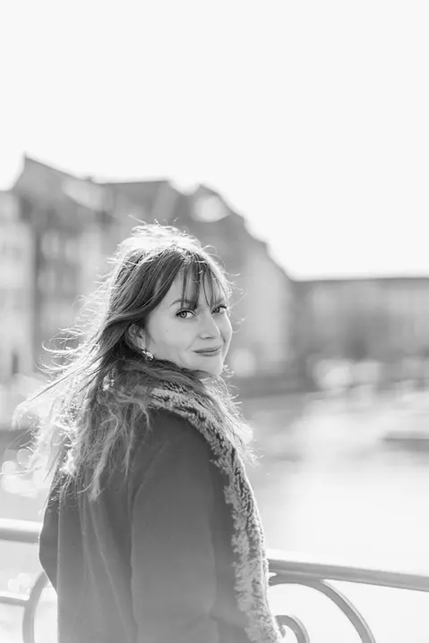 Jeune femme, portrait en noir et blanc se retourne et regarde l'objectif avec un sourire. Lors d'une séance photo portrait lifestyle à Strasbourg. 