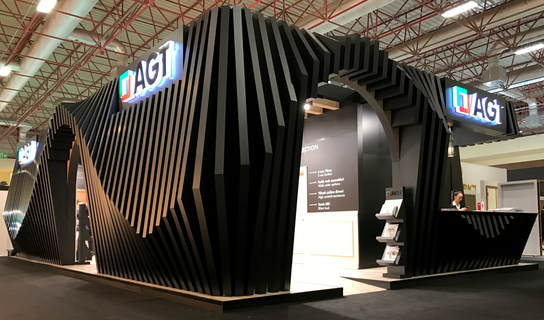 Entrance to AGT exhibition stand with glowing logo, black reception desk, and arch entryway.
