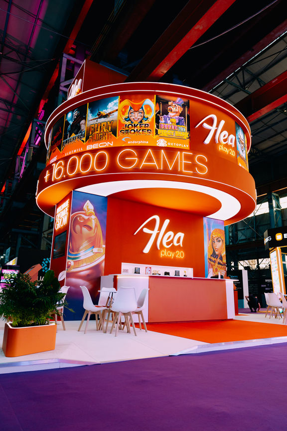 Diagonal view of Alea Play 2.0 stand with tall circular crown, bright lights, and open seating.