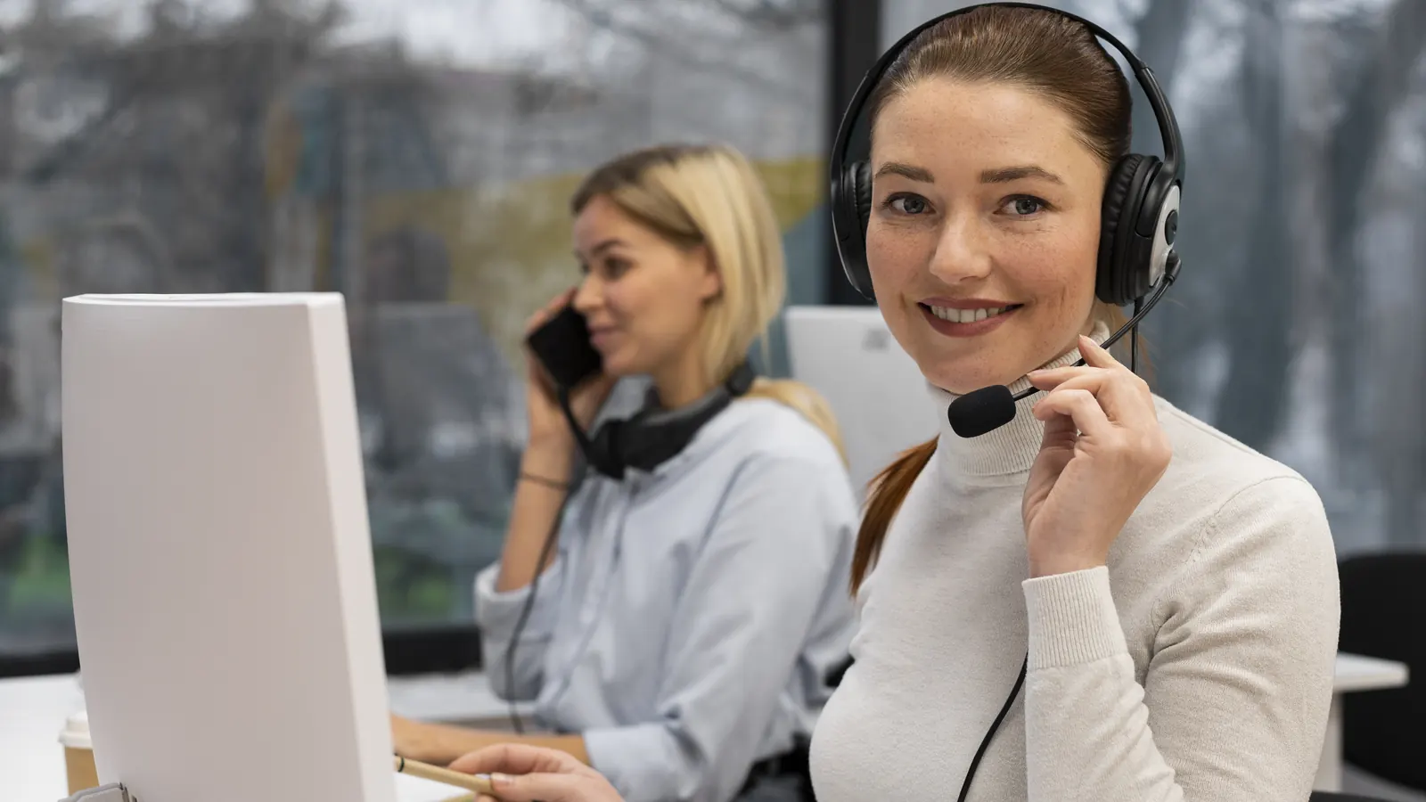 Zwei Mitarbeiterinnen im Kundenservice am Bildschirm, eine mit Headset, eine am Telefon