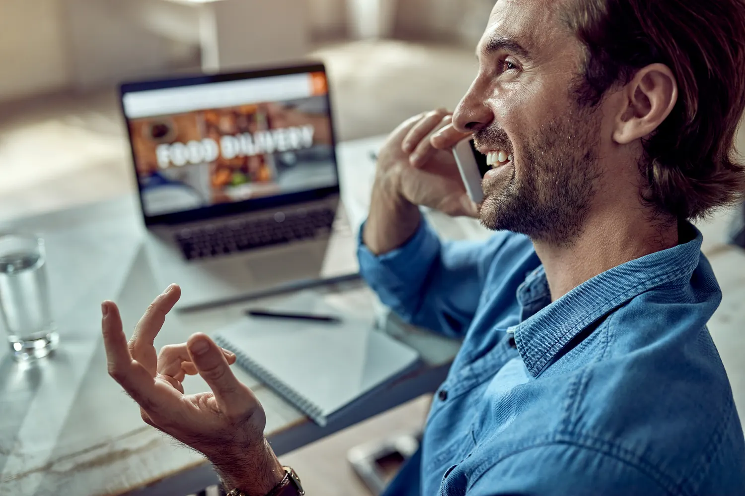 Mann telefoniert erleichtert an seinem Schreibtisch, vor ihm ein Laptop mit geöffneter Website