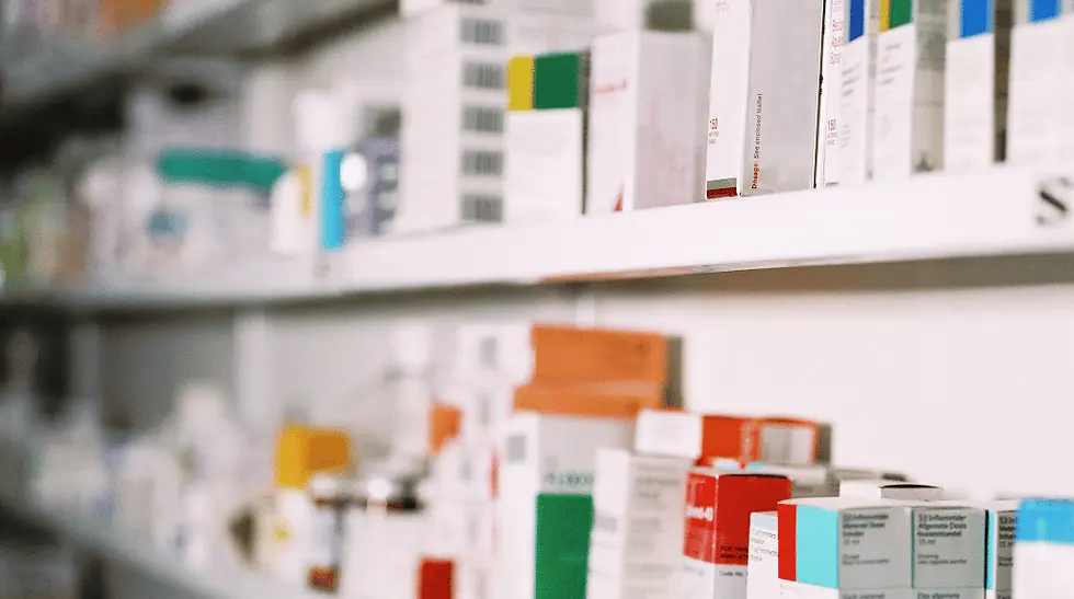Estanterías de farmacia con cajas de medicamentos blancas y de colores, en primer plano, con fondo desenfocado.