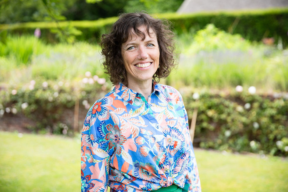 Smiling woman in floral shirt with garden background; outdoor portrait shot.