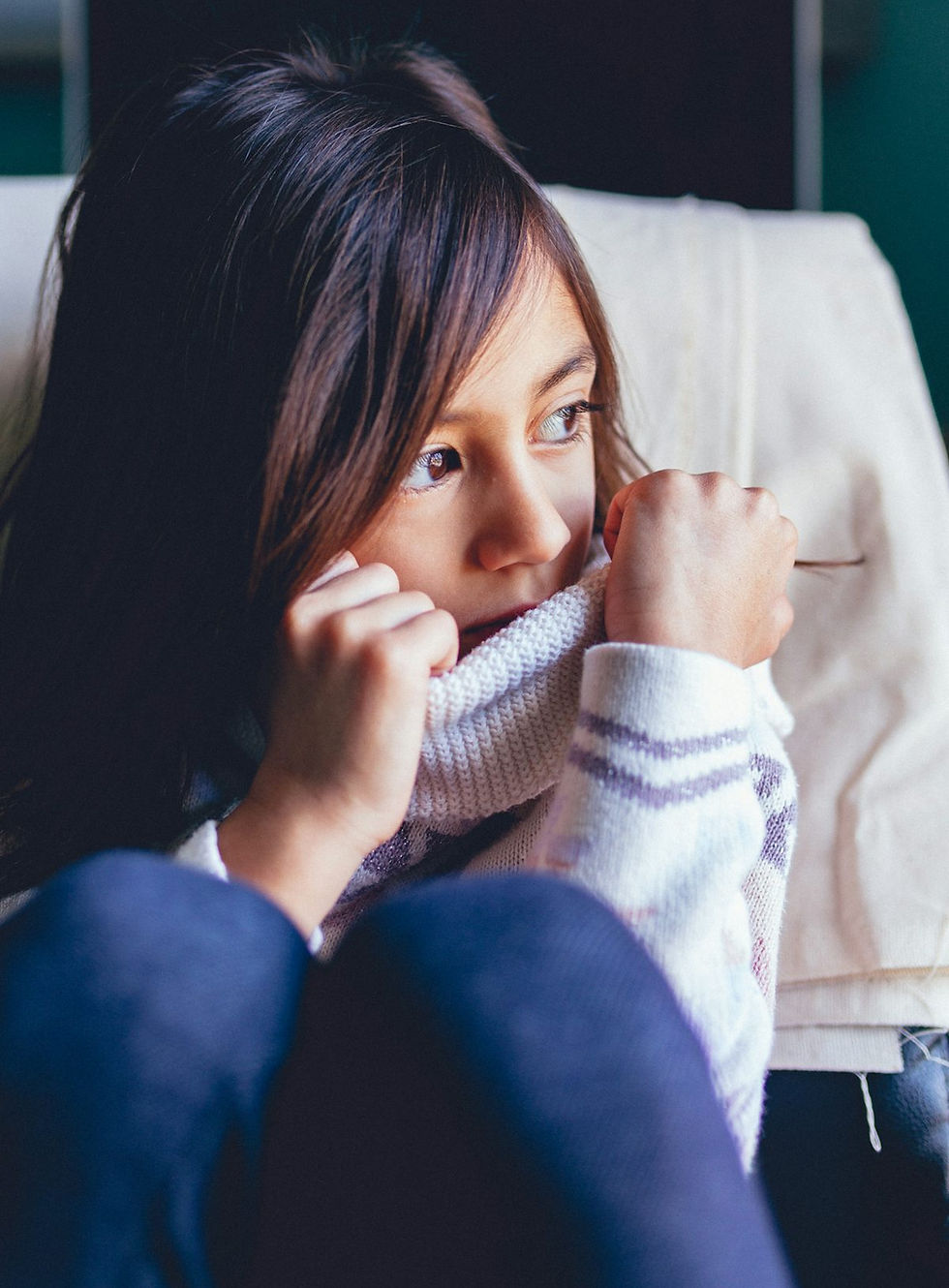 A child looking out a window with fear in her eyes and a shirt pulled over her face