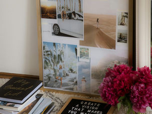A vision board and books on a floor with flowers and a sign tthat says CREATE A VISION THAT MAKES YOU WANNA JUMP OUT OF BED IN THE MORNING