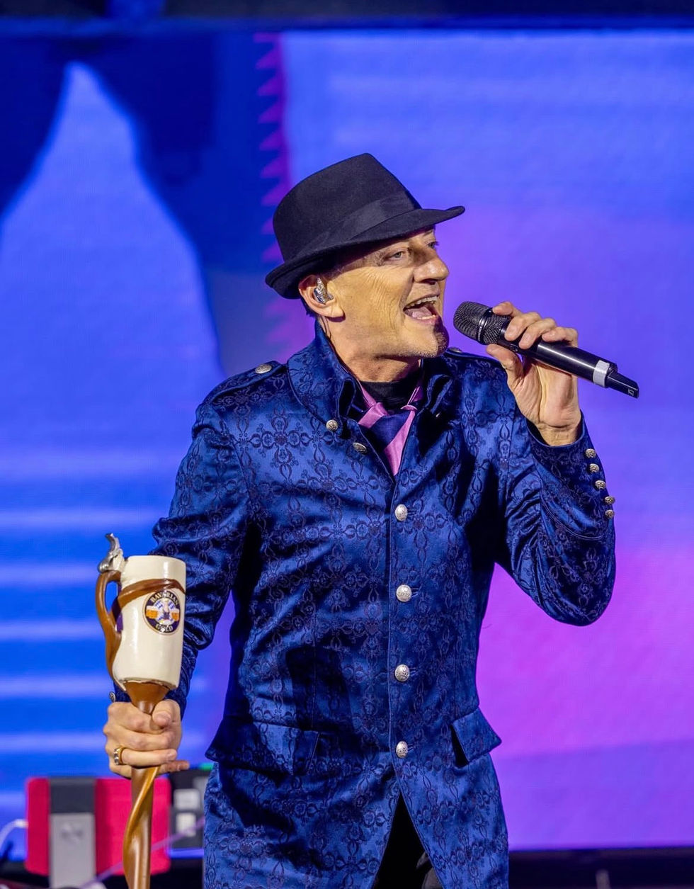 Man in blue jacket singing, holding a trophy.