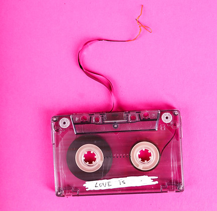 A cassette tape with it's reel unwound sits against a pink background