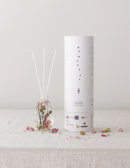 WAMOGA29のハーバリウムディフューザー（ローズ）と円筒パッケージを並べた、プロダクトとビジュアルアイデンティティを一体で設計したブランディングデザイン実例写真です。