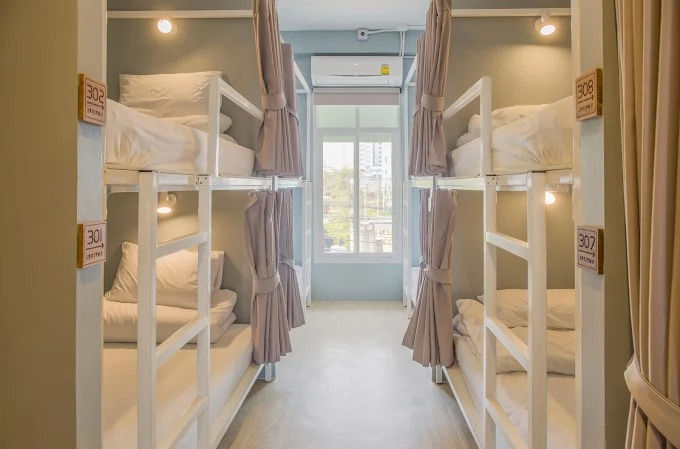 Ekanake Hotel's Bright dorm room with white bunk beds, curtains, and room labels 301, 306, 307, 308 beside a window.