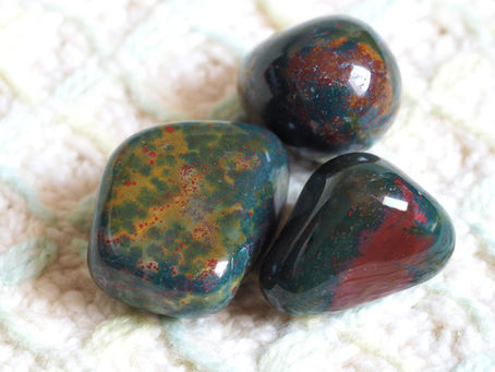 Photographie de trois pierres d'héliotrope polies, une variété de jaspe vert avec des taches d'hématite rouge, connue sous le nom de 'pierre de sang'.