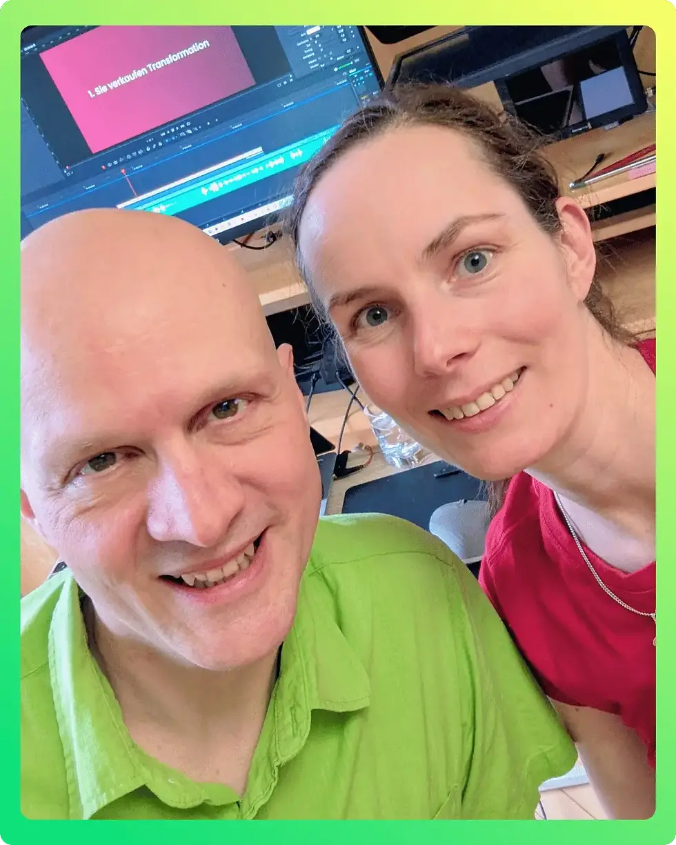 Two people smiling, one in a green shirt, the other in red. A computer screen shows editing software and text: "Sie vertrauen Transformation."