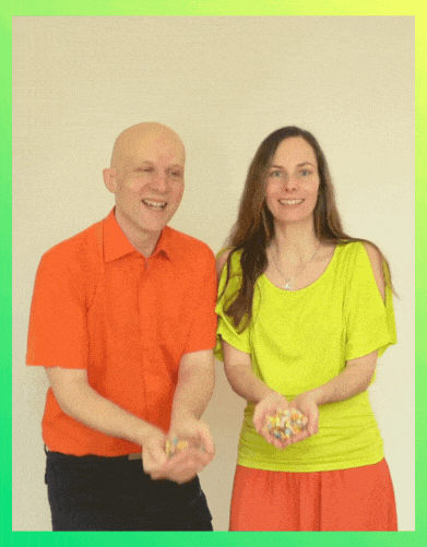 Sandor Kersting im orangefarbenen Hemd und Conny Jost im neongelben Oberteil mit orangefarbenem Rock lächeln, während sie beide Konfetti in den Händen halten und in die Luft werfen.