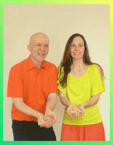Sandor Kersting im orangefarbenen Hemd und Conny Jost im neongelben Oberteil mit orangefarbenem Rock lächeln, während sie beide Konfetti in den Händen halten und in die Luft werfen.