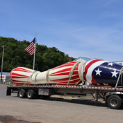 red and white painted drums along side an American flag painted drum on a truck ready to be shipped