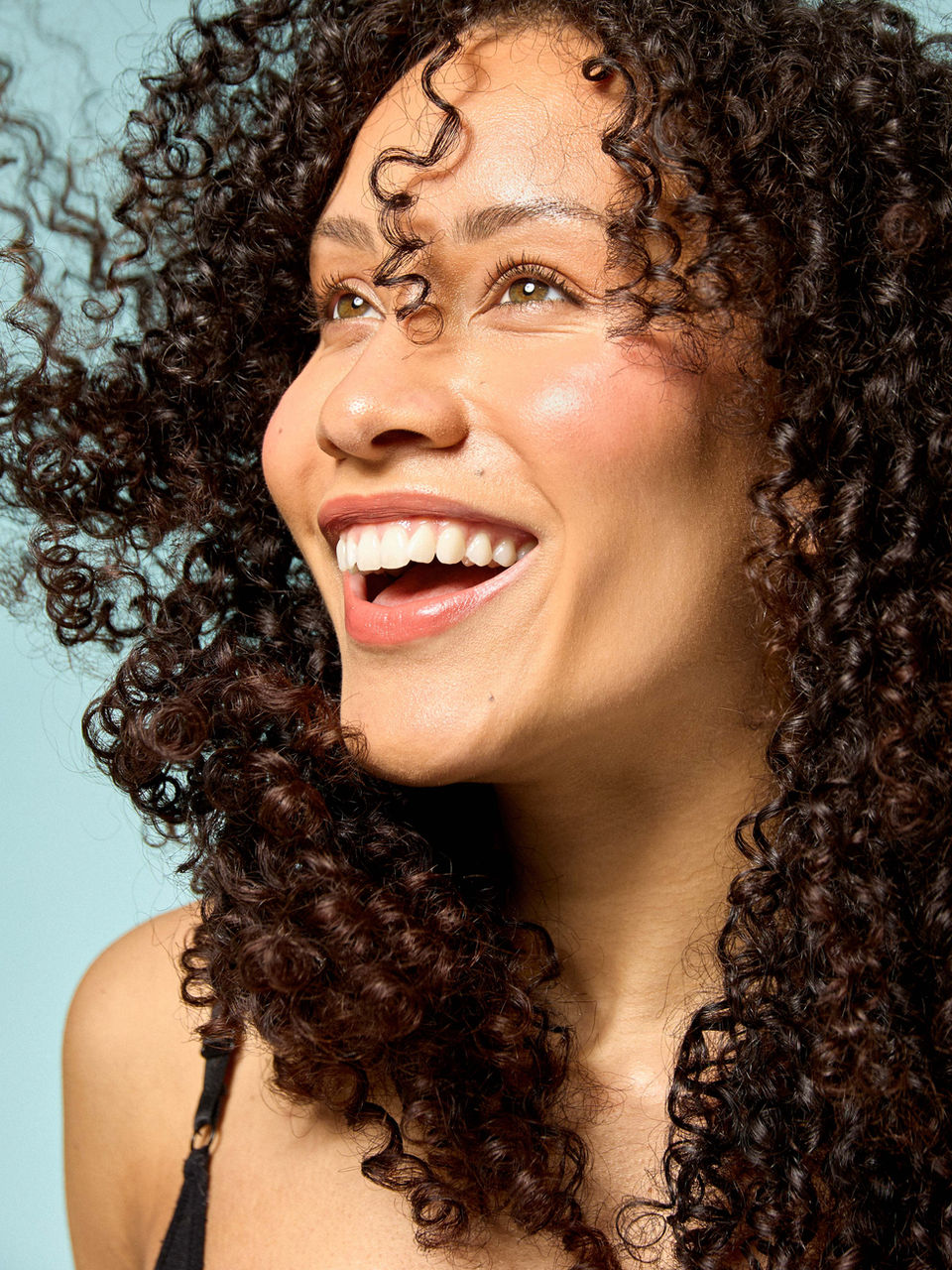 model with curly hair laughing side profile teal background