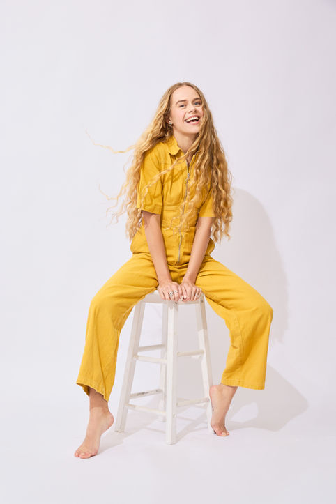 model in yellow jumpsuit seated on stool with wind blowing in hair