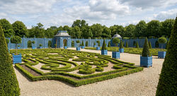 A sweeping view of a magnificent French formal garden featuring intricate boxwood parterres, a grand
