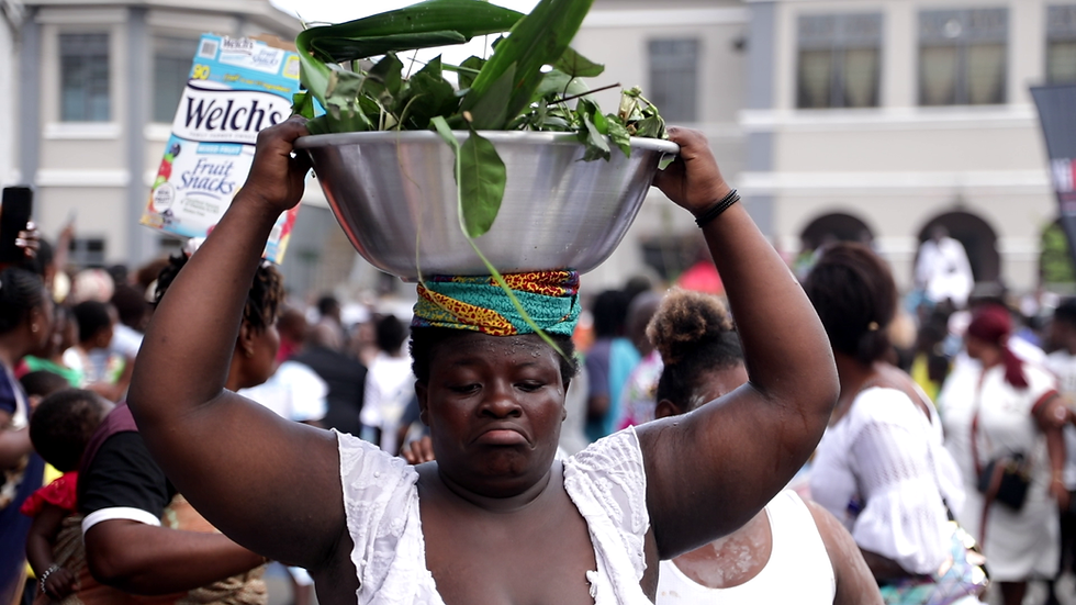 A proud mother of twins walks through the bustling streets, balancing a traditional bowl on her head—a symbol of her unique status in the community of Jamestown.