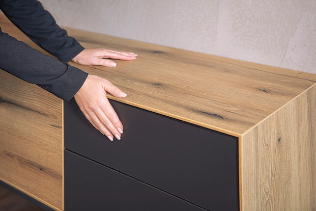 Hände berühren modernes Sideboard, Holzoptik und Anthrazitfronten zeigend.
