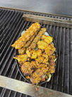 A grill with a variety of food items cooking on it, including meats, vegetables, and seafood.