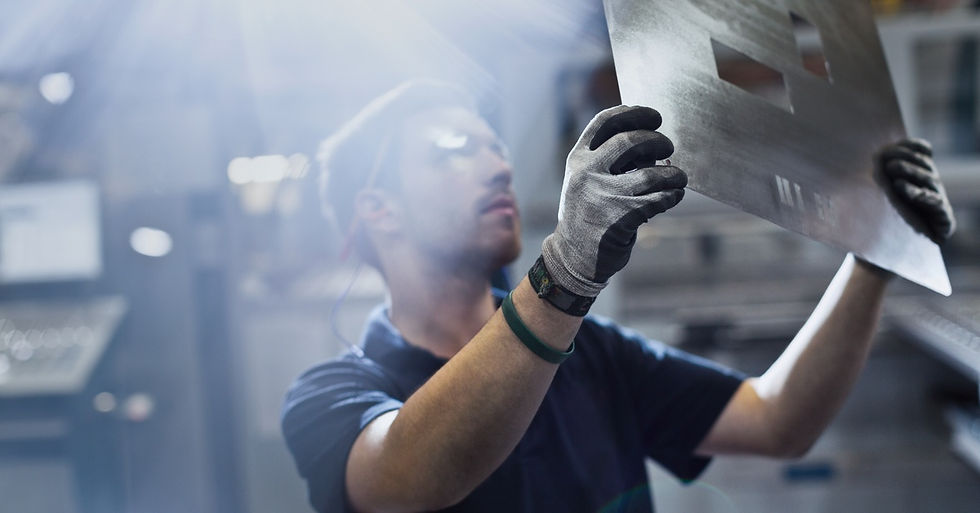 A metal fabrication professional holding up a sheet of metal with several rectangular cutouts on the surface.