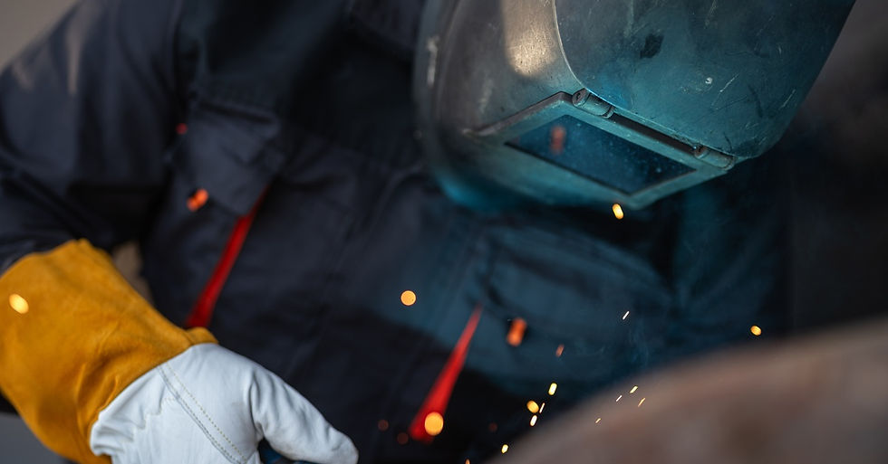 A worker wearing a protective mask and gloves standing over a metal structure during a fabrication project.