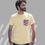 Thumbnail: Guy wearing a pale yellow t-shirt with a design printed on a faux pocket