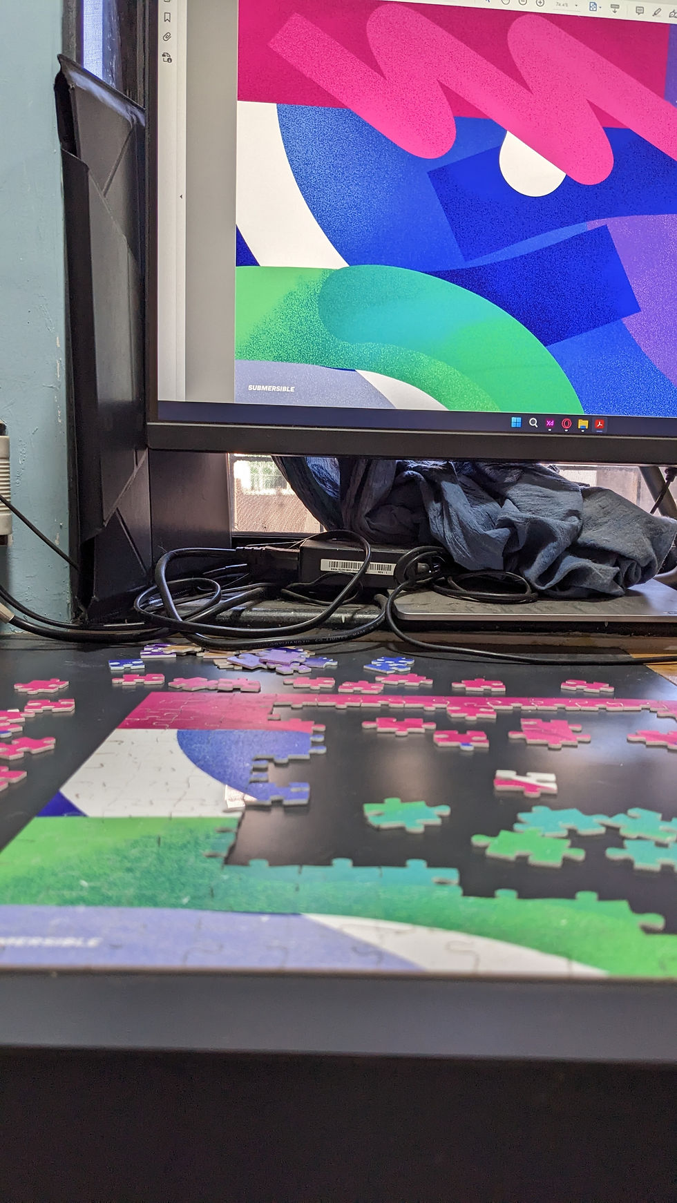 Picture showing jigsaw puzzle design on screen while someone works on it on the table alongside