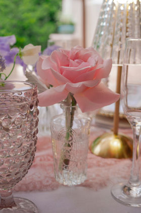 Elegant bridal shower place setting featuring a blush rose bud vase, pink goblets, and LED table lamp.