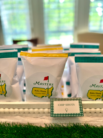 Custom food display featuring Masters-inspired chip bags, themed signage, and event styling for a baby shower in The Woodlands.