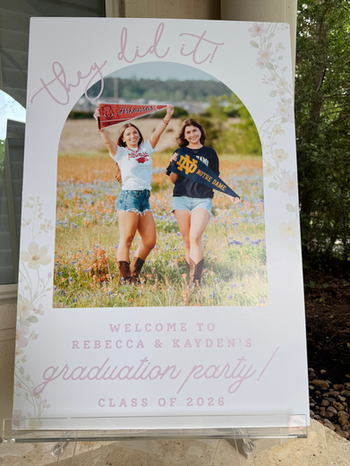 Custom graduation welcome sign with graphic design displayed on a clear acrylic easel for a spring graduation party.