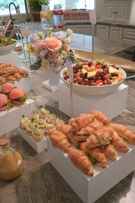 Bridal brunch food display featuring tea sandwiches, fruit salad, fresh florals, and acrylic risers.