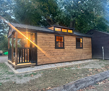 Cozy tiny house with wooden exterior, glowing lights, and a small porch.