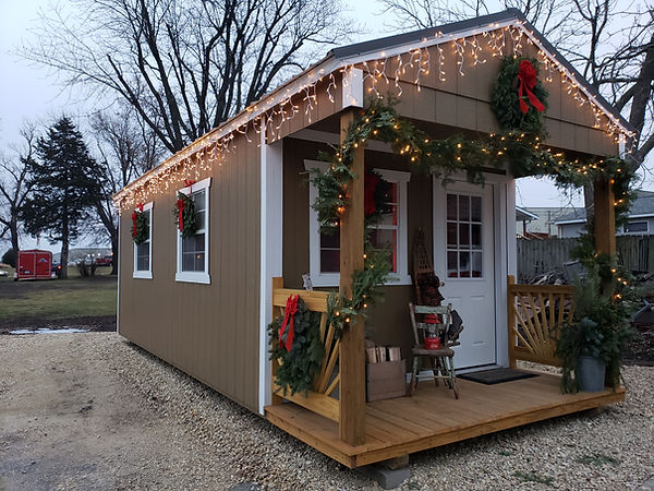 Small brown shed decorated for Christmas with lights, wreaths, and garland.