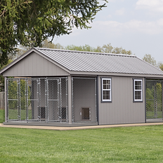 Large gray outdoor shed with multiple dog kennels in lush backyard.