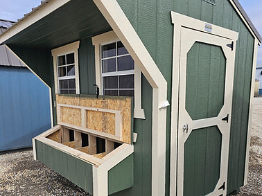 Green wooden chicken coop with white trim, nesting boxes, and side door.