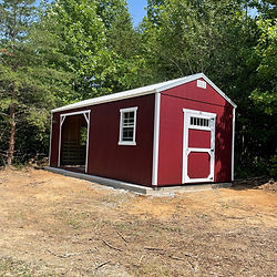 Red shed with white trim, a porch, and window among trees.
