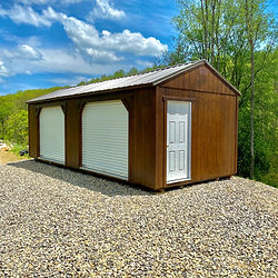 Brown Metal Building, white garage doors, gravel lot, green trees.