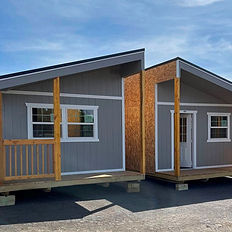 Two gray modular cabins with wooden porches under blue sky.