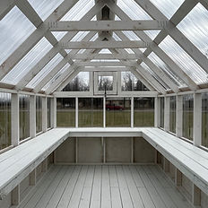White wooden greenhouse interior with clear roof panels and long benches.